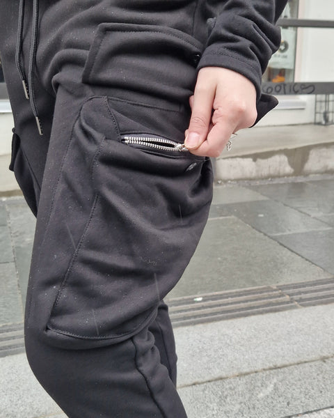 Benjamin and Signe standing side by side on the Tromsø high-street next to Rein Love Brand Store wearing black cargo pants and black sweat shirts. The male model is on the right and the female model is on the left.